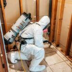 A person wearing a personal protective Tyvek suit and respirator HEPA vacuuming asbestos fiber contamination.
